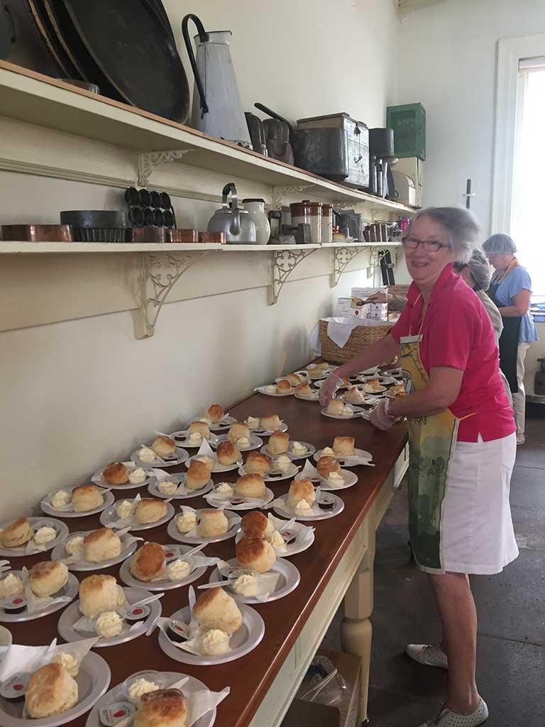 plates of scones lined up on kitchen bench with CWA helpers laughing happily